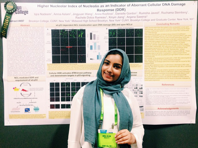 Amna Aslam standing in front of the poster she contributed to