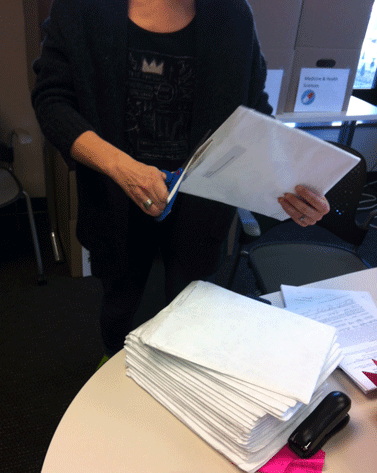 Animated GIF of a CUNY employee opening a white envelope containing a research paper for NYCSEF. A pile of similar envelopes is in the foreground.