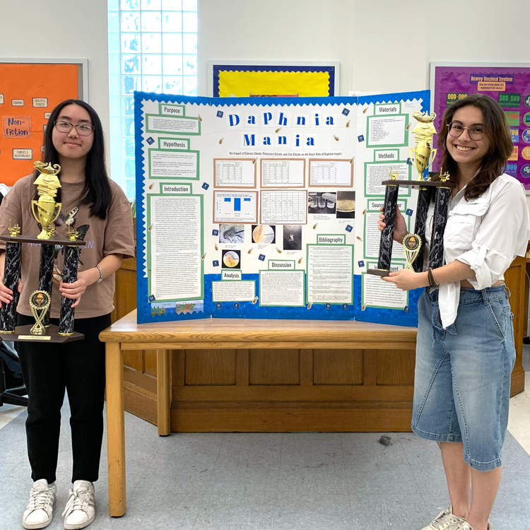 Students standing in fron of their poster holding trophies